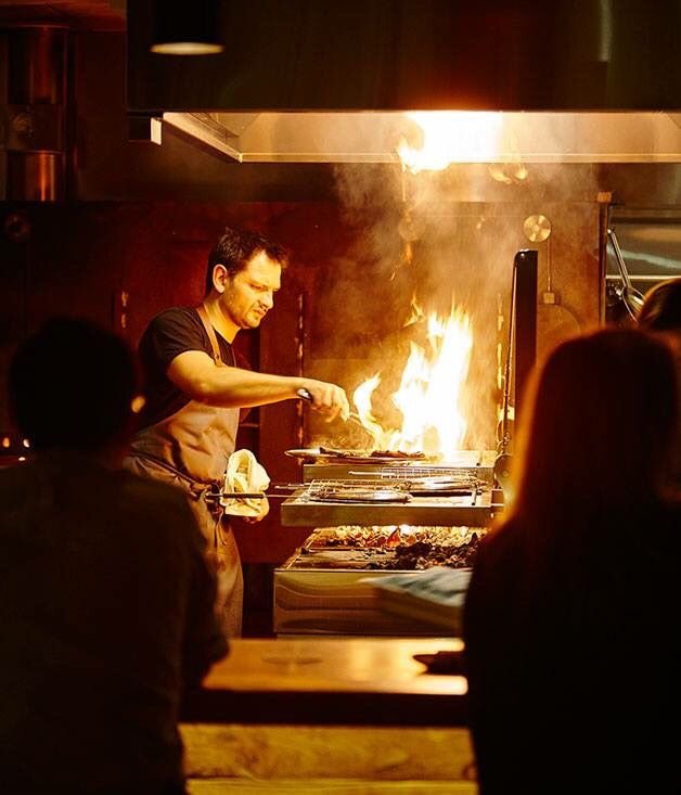 Chef concentrado cozinhando em chapa com labaredas altas, representando alta demanda